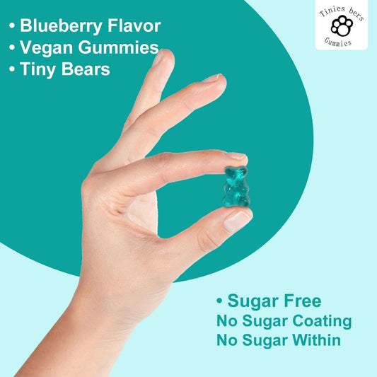 Hand holding a blue sugar-free vegan gummy bear with blueberry flavor, labeled as Tiny Bears Gummies.